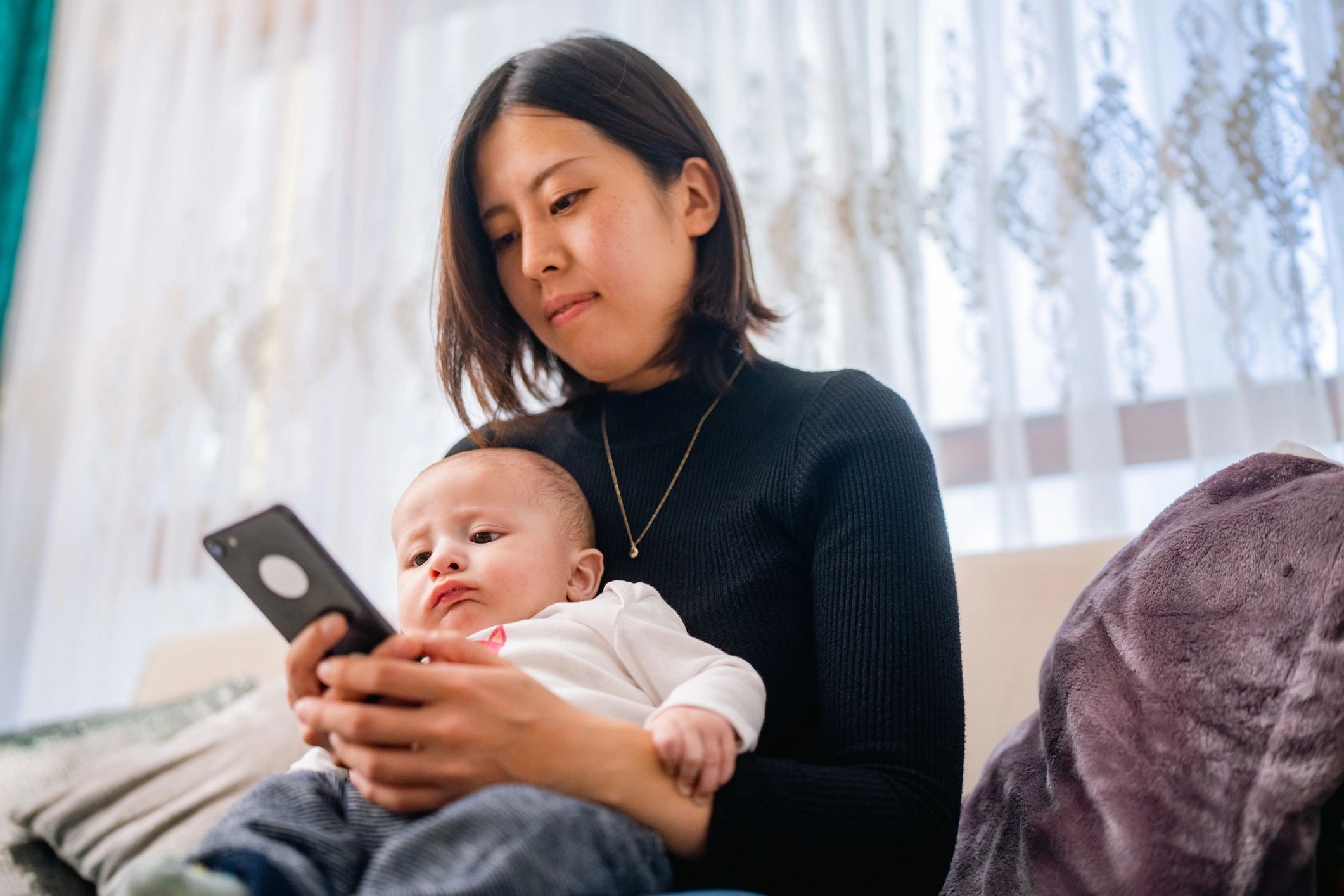 Mother holding her baby while using a smartphone at home