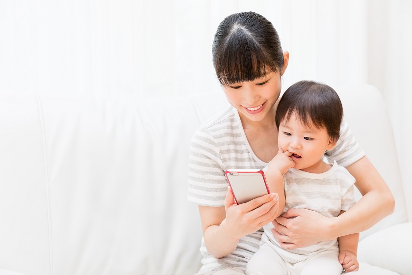 Mother holding a baby while using a smartphone