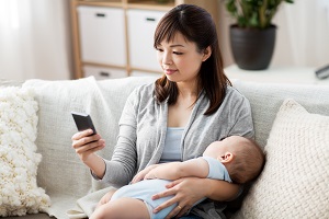 Mother holding her baby while using a smartphone